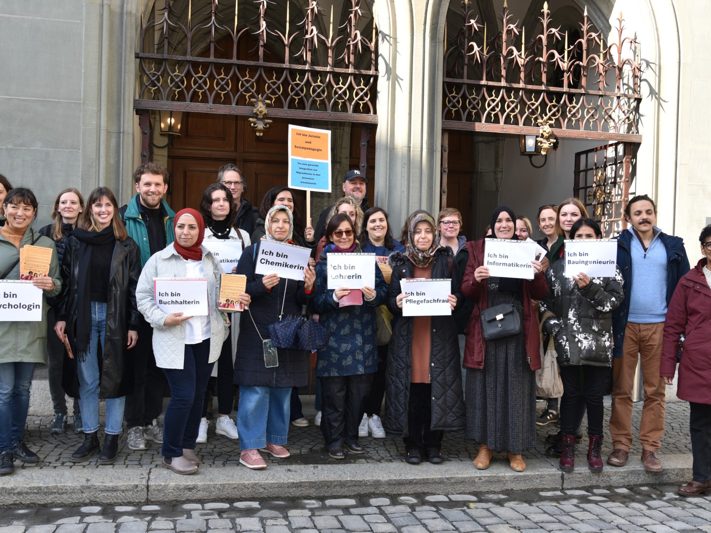 Frauen mit Migrationshintergrund halten Schilder mit Berufsbezeichnungen während einer Demo in Bern