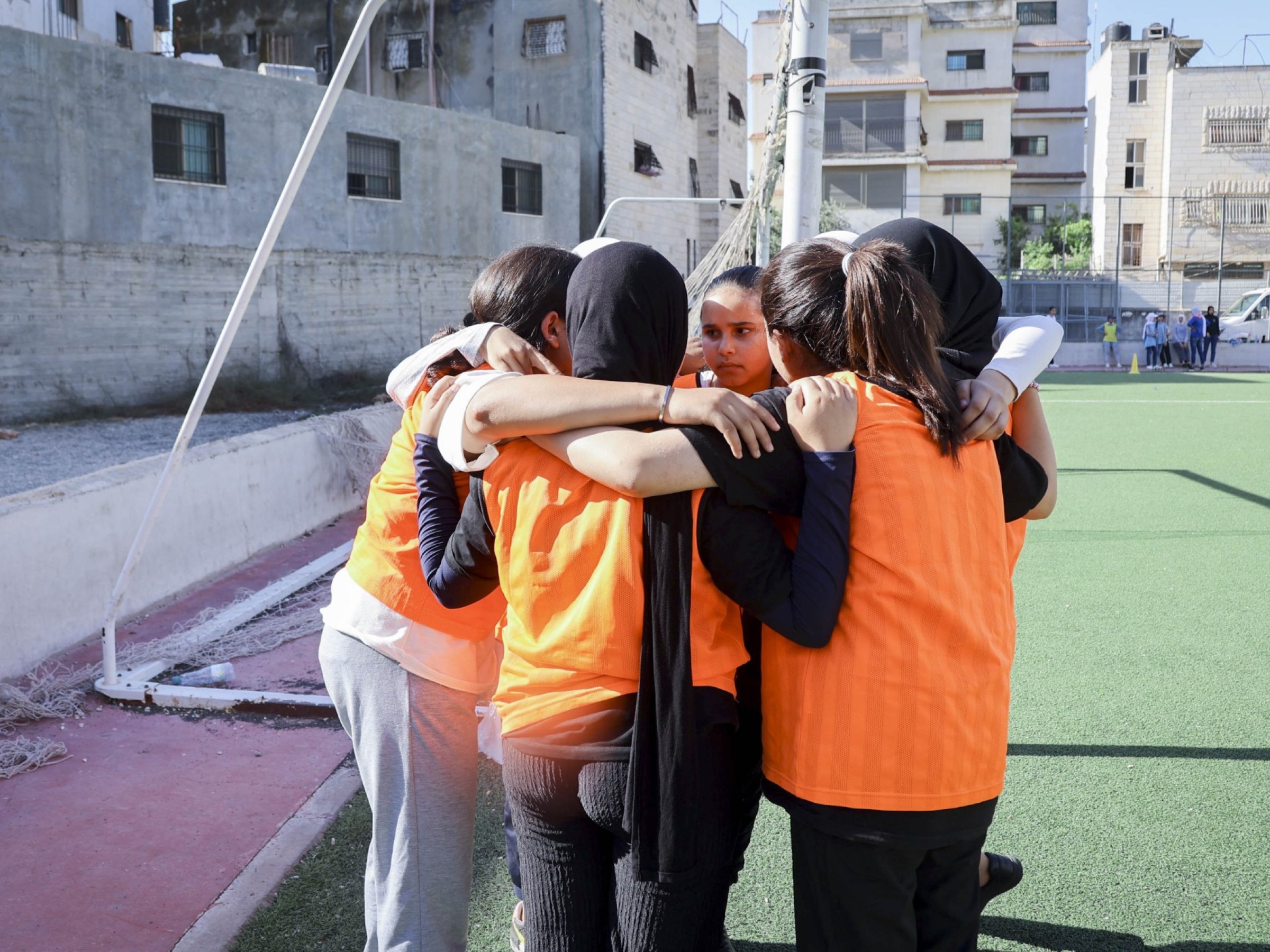 Junge Mädchen mit orangen Trikots stehen in einem Kreis und halten sich fest