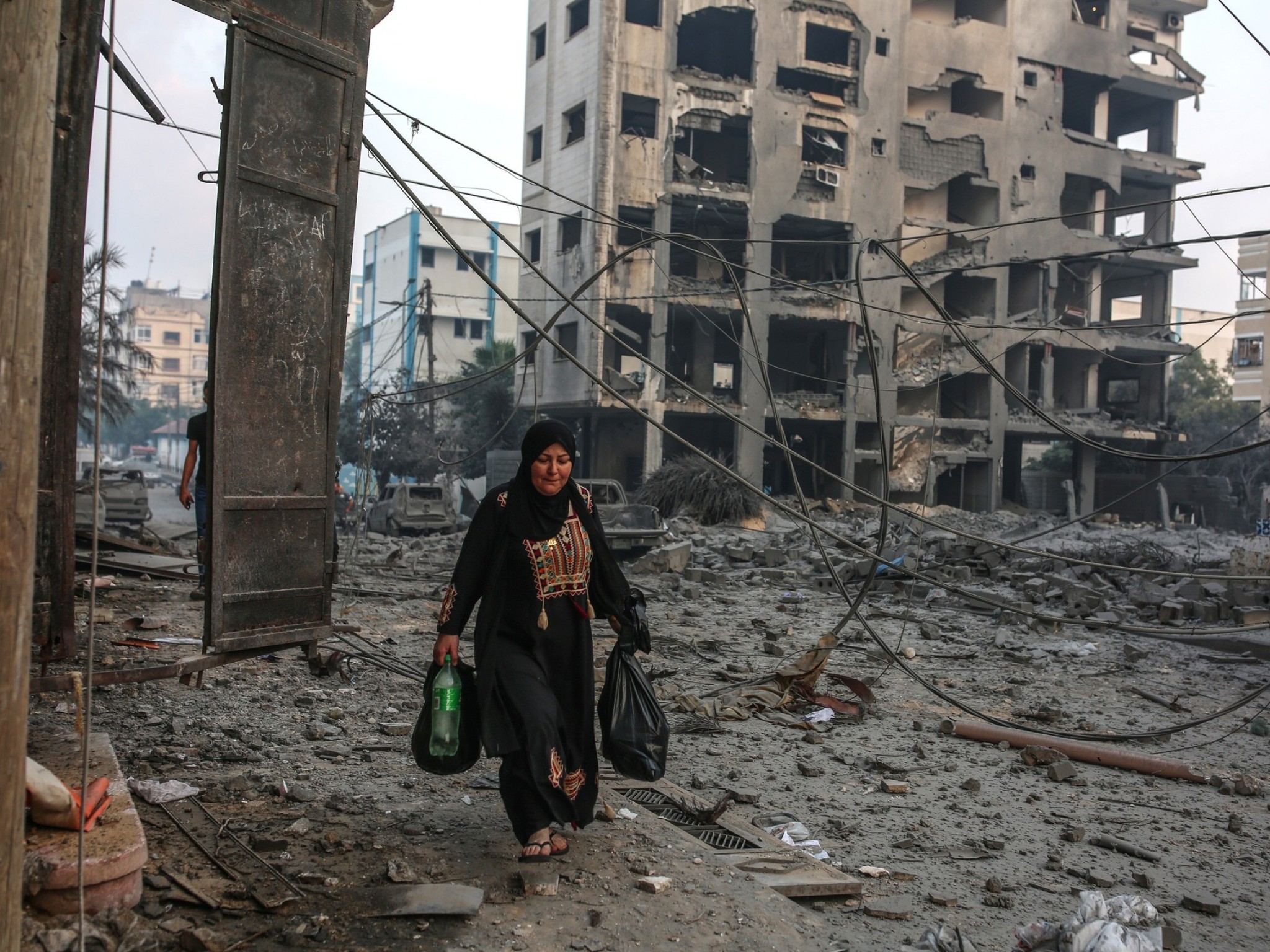 Frau mit zwei Säcken in der Hand läuft im zerstörten Gaza herum.