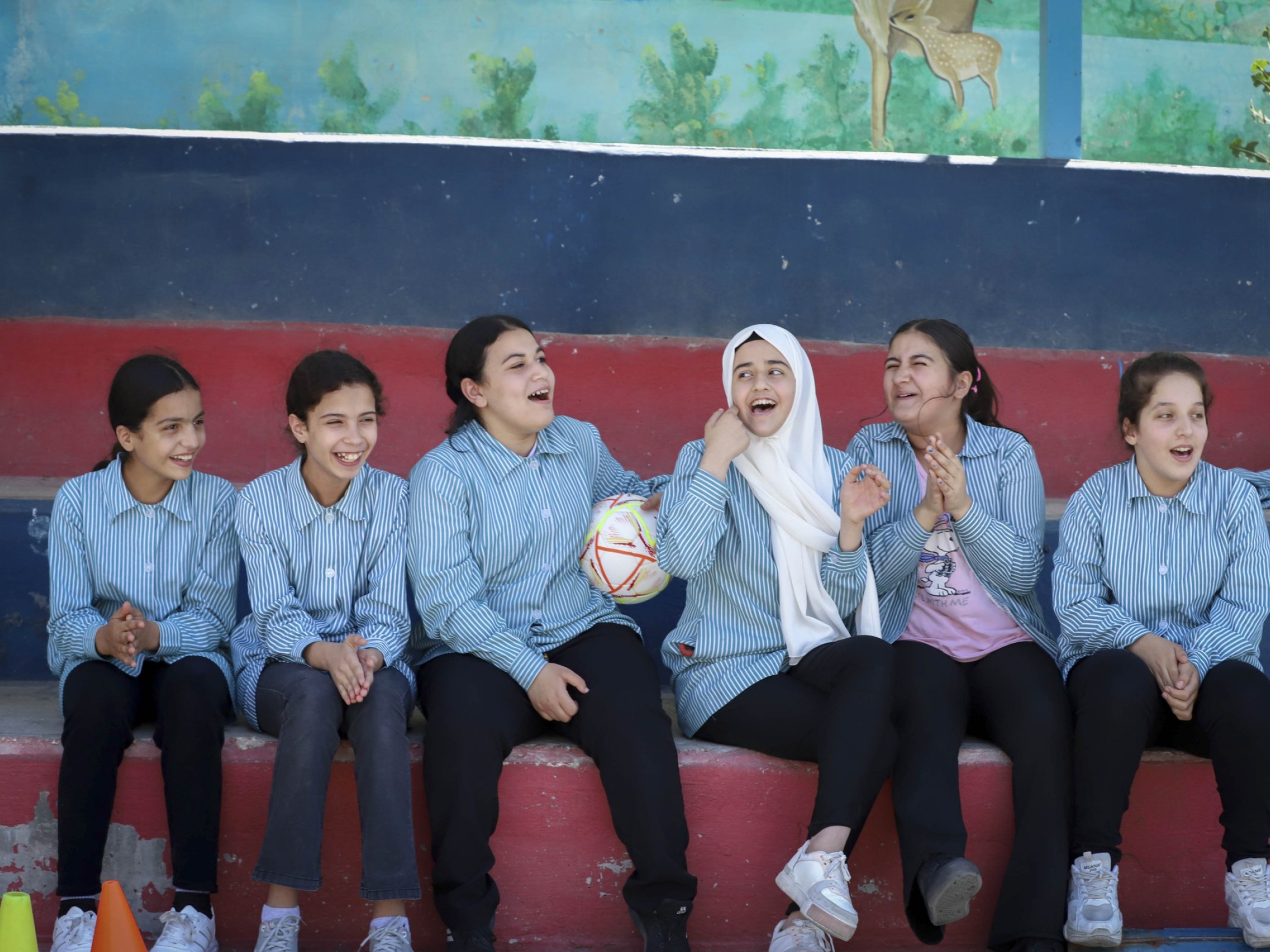 Mädchen aus Palästina sitzen auf der Wartebank beim Fussballspiel und lachen.